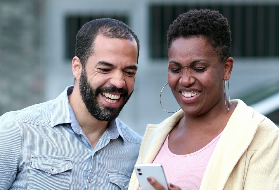 Two TACT foster carers smiling whilst looking at a mobile phone