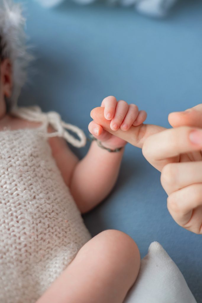A newborn baby holding an adult's finger